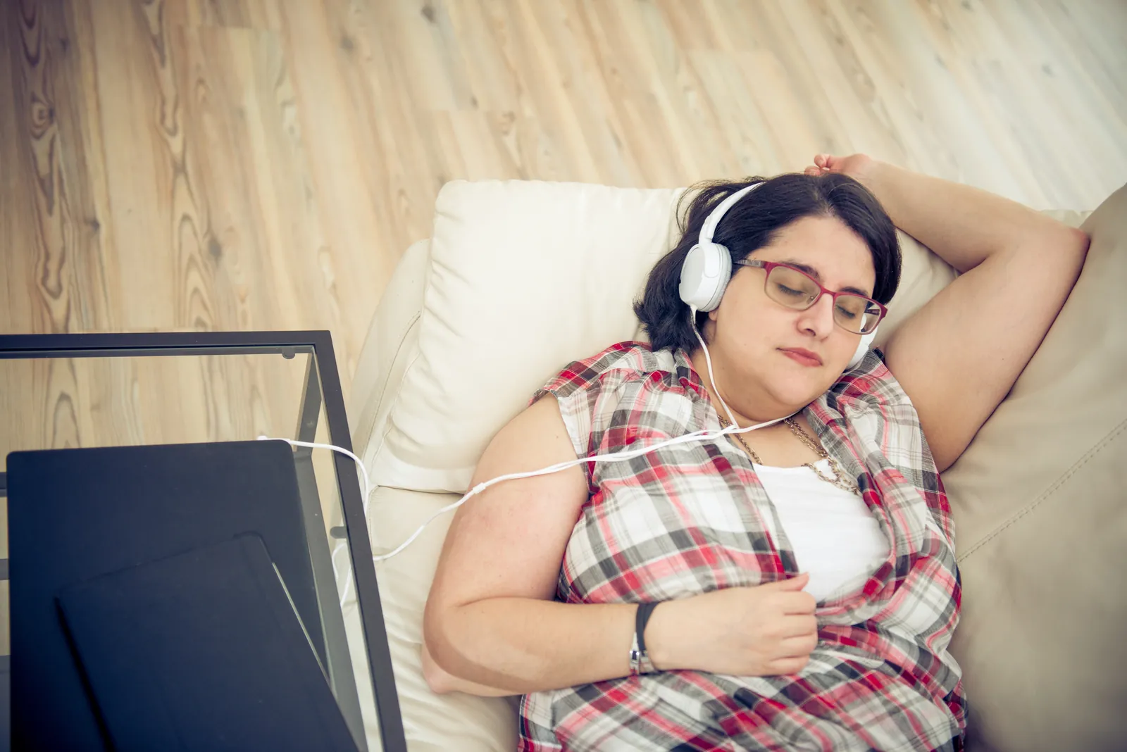 Femme allongée sur un canapé, les yeux fermés, un casque sur les oreilles